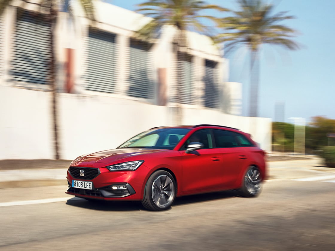 A red seat leon sportstourer benefits of seat’s service and maintenance plan, in motion in a residential area with a house and palm trees.