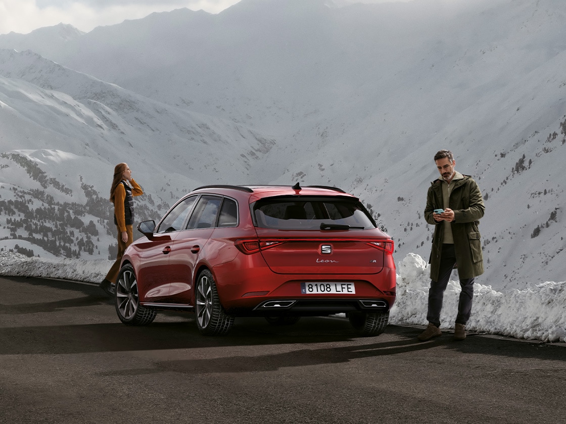 A red seat leon Sportstourer car parked on a mountain road waiting for seat service mobility and roadside assistance benefits. Two people standing nearby.