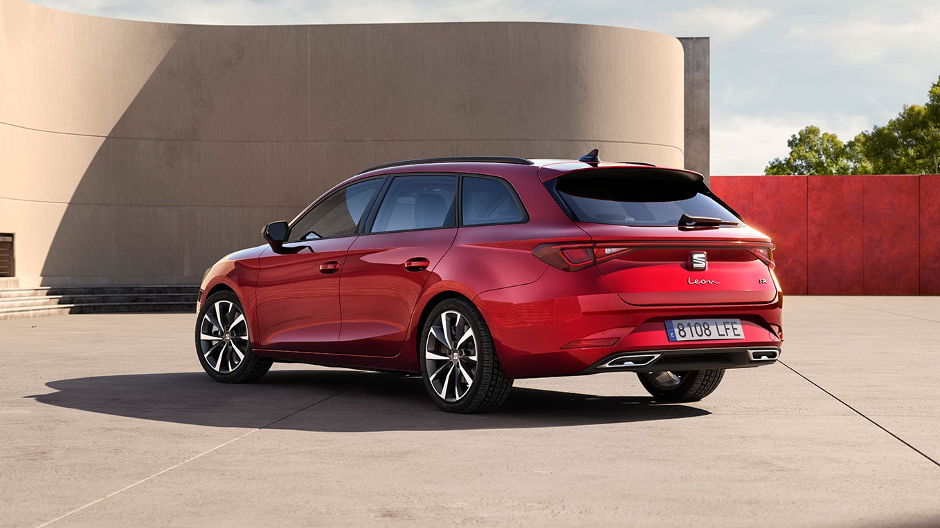 Side rear view of the seat estate car, the seat leon sportstourer in desire red, parked facing the wall of a building in an outdoors setting. The view showcases the rear design of the car.